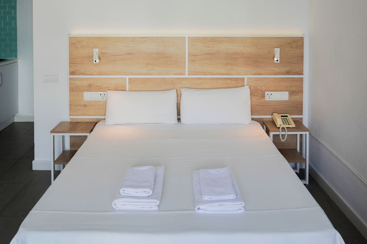 A hotel room with a large bed, two bedside tables, a wooden headboard, and a telephone on one of the tables.