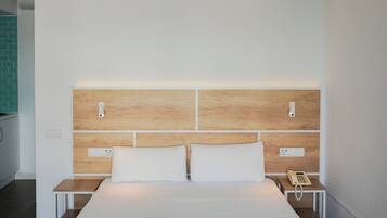 Habitación de hotel con una cama grande, dos mesitas de noche, un cabecero de madera y un teléfono sobre una de las mesitas.