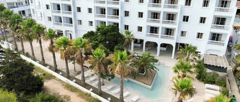 Un hotel de varios pisos con balcones, piscina y palmeras.