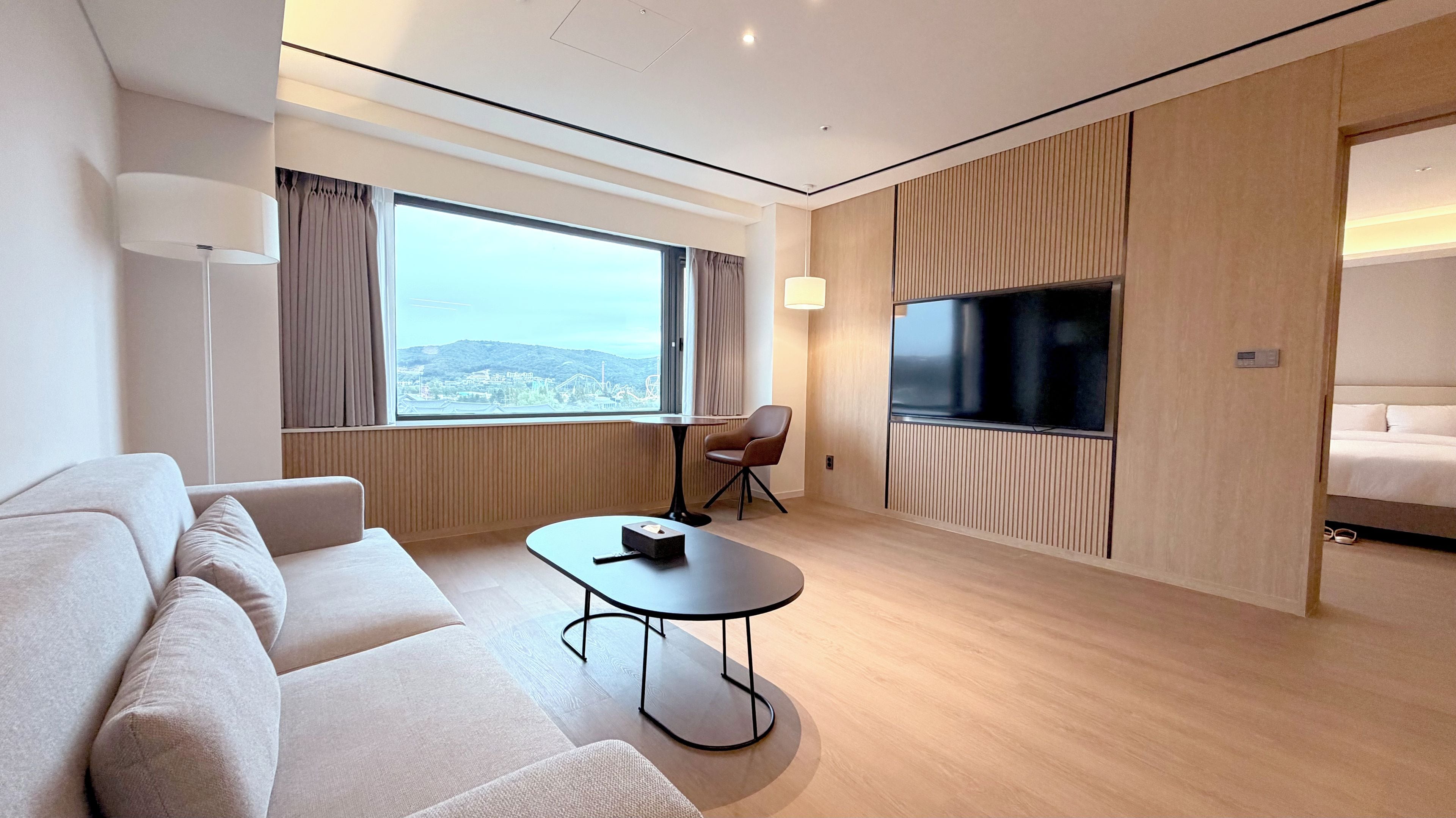 Habitación de hotel moderna con sofá, una mesita, televisor y un ventanal con vistas a la ciudad.
