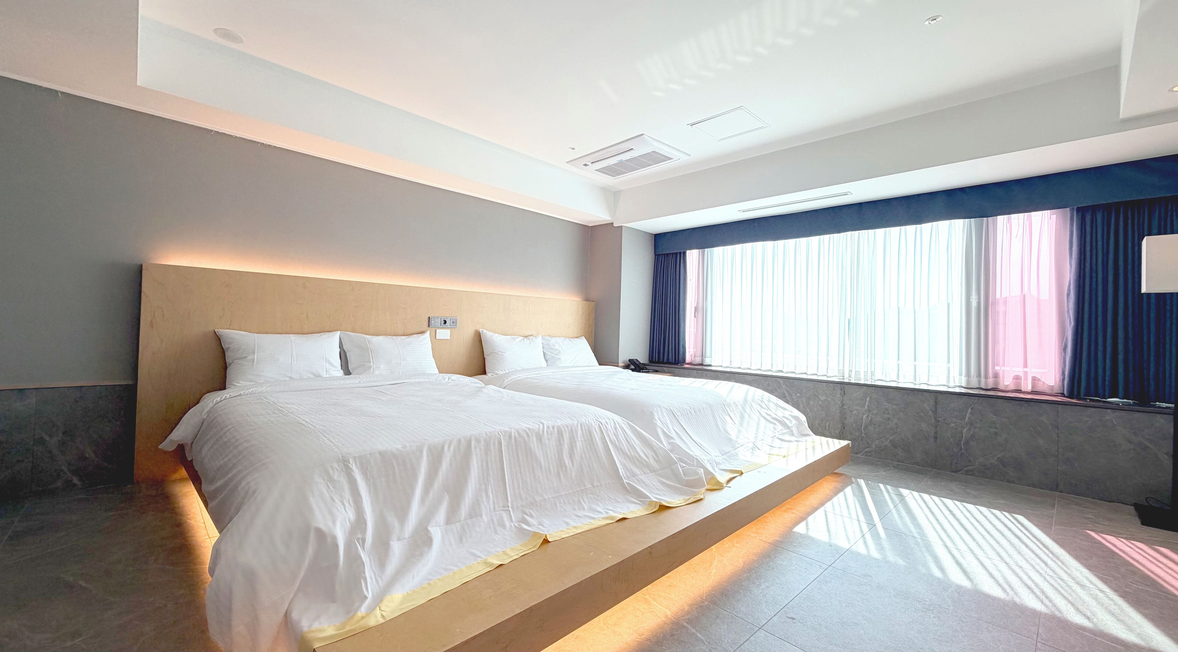 A hotel room with a large bed, a headboard, a bedside table, a telephone, and a window with curtains.
