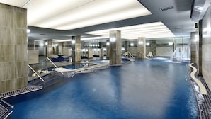 Un área de piscina interior moderna con agua cristalina, múltiples carriles y una fuente central.