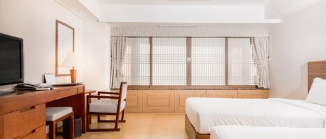 Una habitación de hotel con escritorio de madera, televisor, silla, cama y ventana con cortinas.