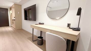 A modern bedroom with a wooden desk, a round mirror, a television, and a trash can.