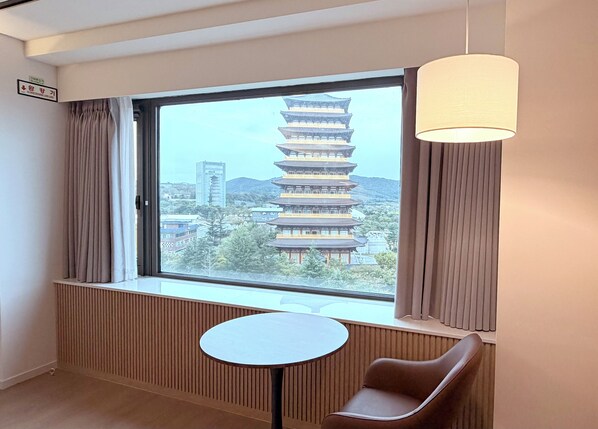 A hotel room with a view of a traditional pagoda, a round table, and a brown chair.