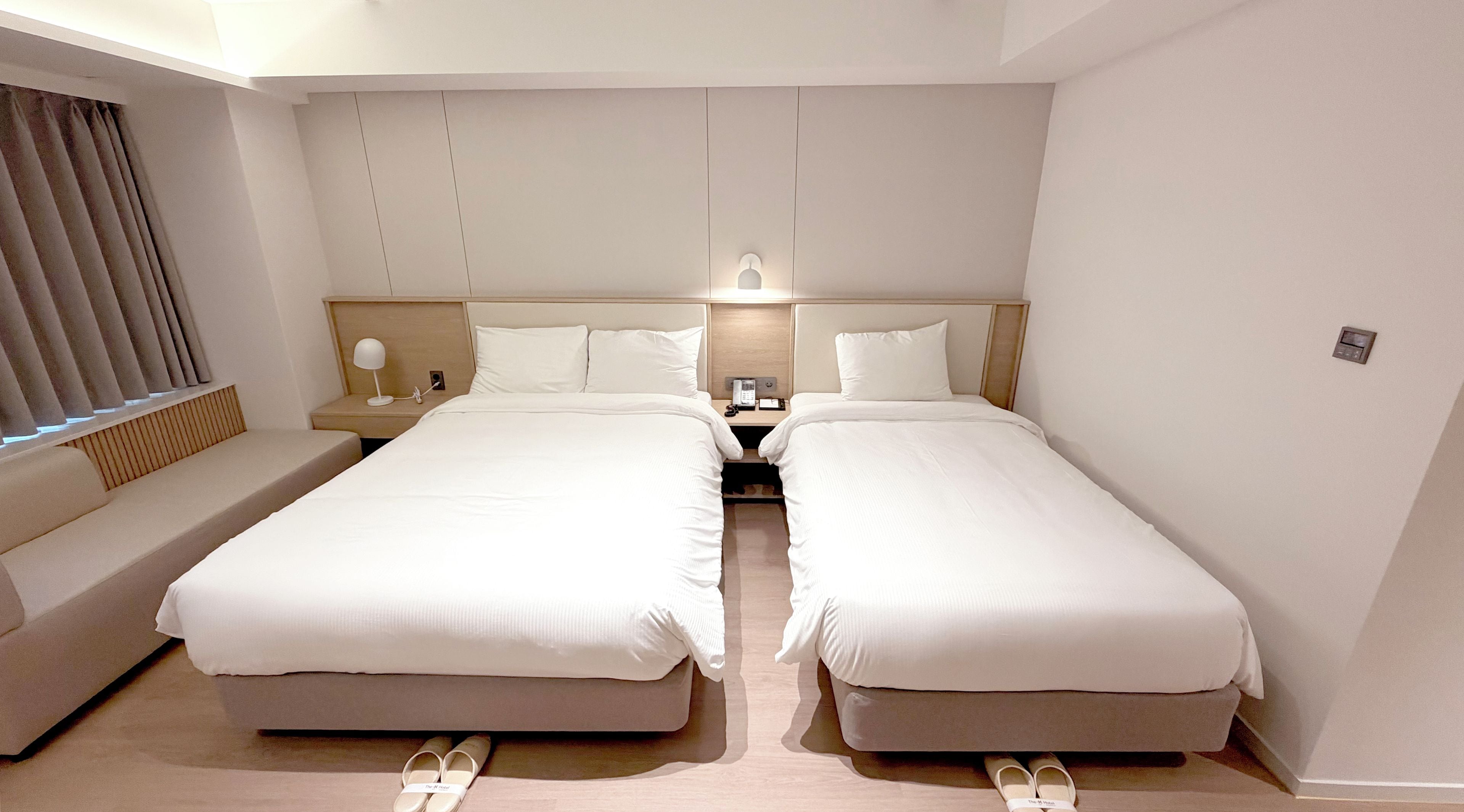 Een hotelkamer met twee bedden, een nachtkastje met een lamp, een telefoon en een wandlamp.