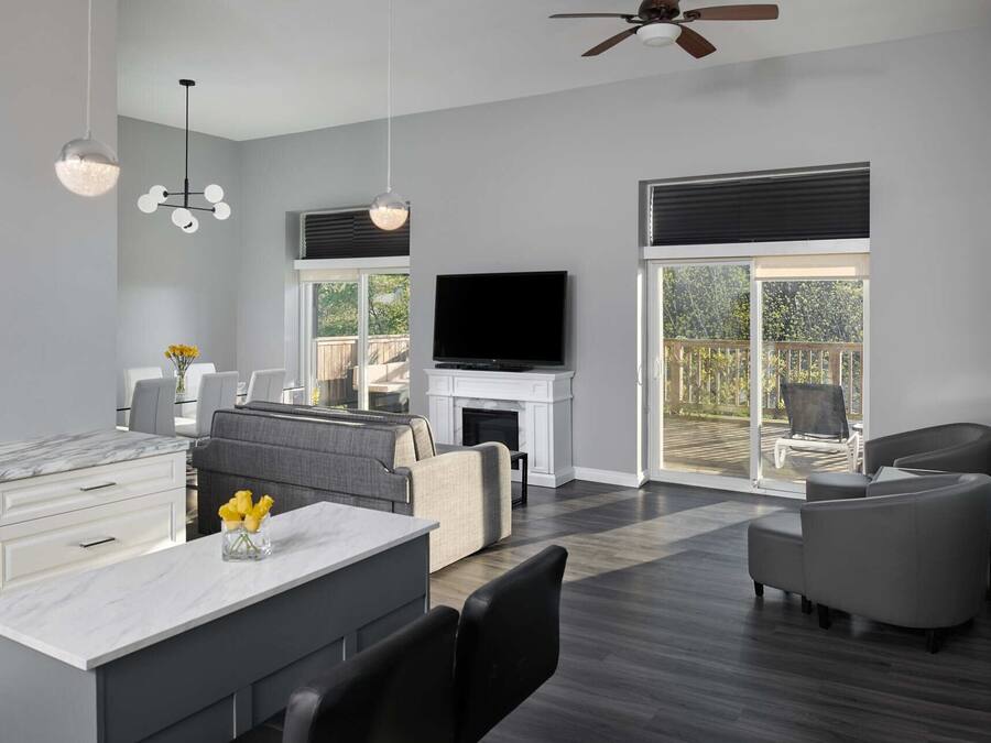 A modern living room with a fireplace, a flat-screen TV, and a balcony with a view of trees.