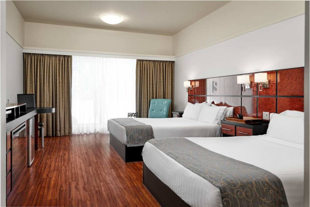 A hotel room with two beds, a desk, a chair, and a minibar.