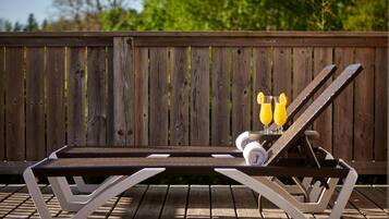 Une chaise longue avec une structure en métal et un siège en bois, placée sur une terrasse en bois, avec une clôture en bois en arrière-plan.