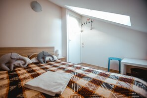 Un dormitorio con cama, almohadas, una colcha, un taburete pequeño y un tragaluz.