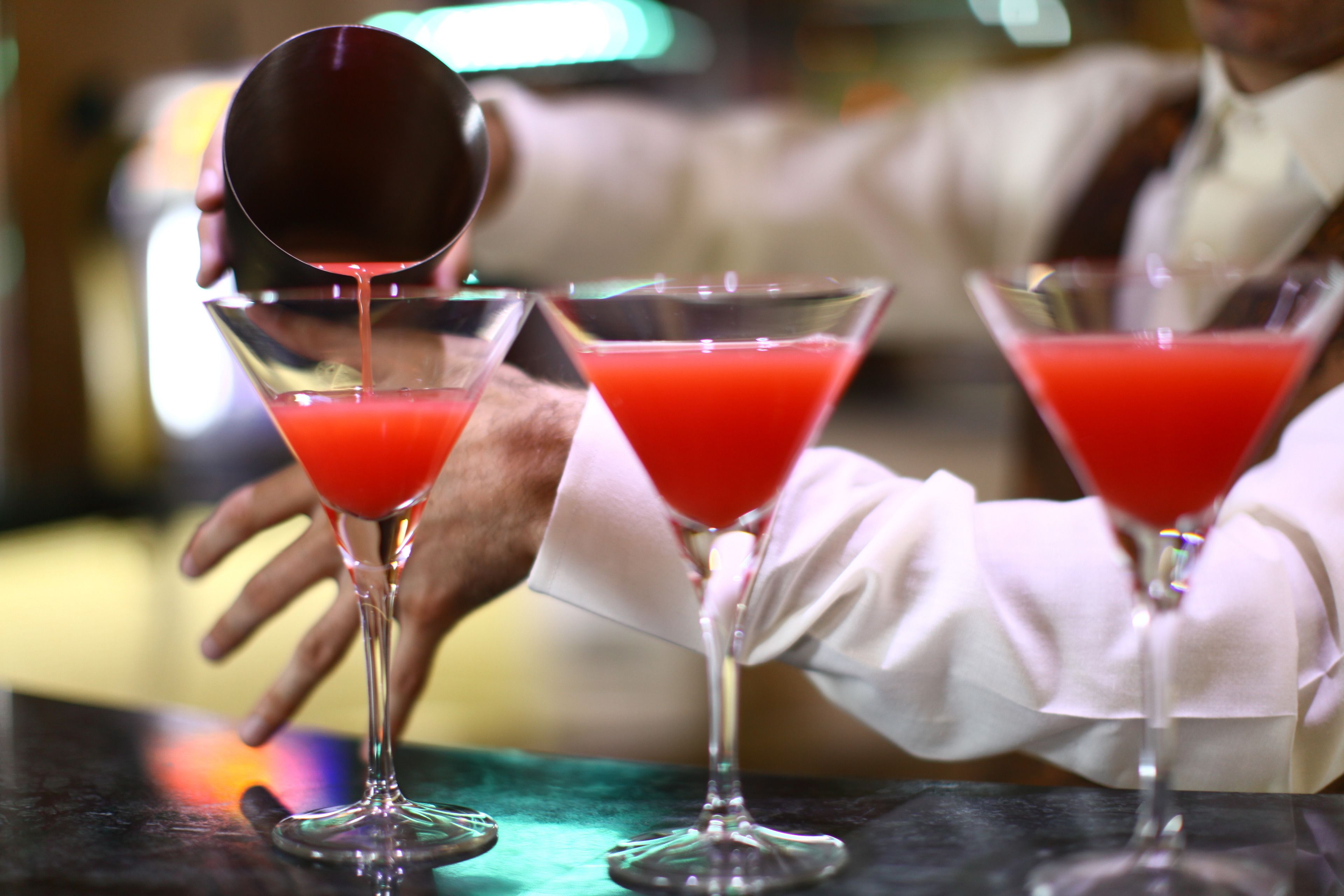 A bartender pouring a red drink into a martini glass.