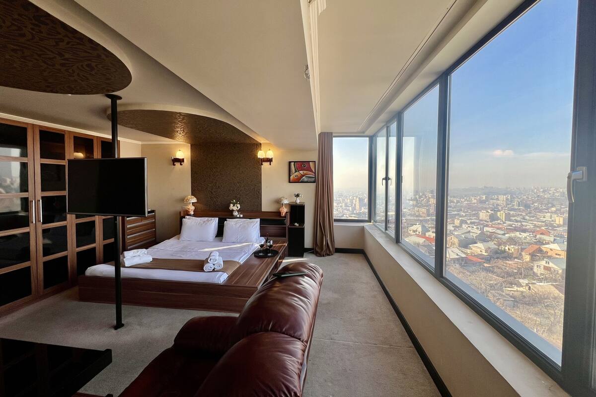 Une chambre d’hôtel avec un grand lit, une télévision, un canapé et une vue sur la ville.
