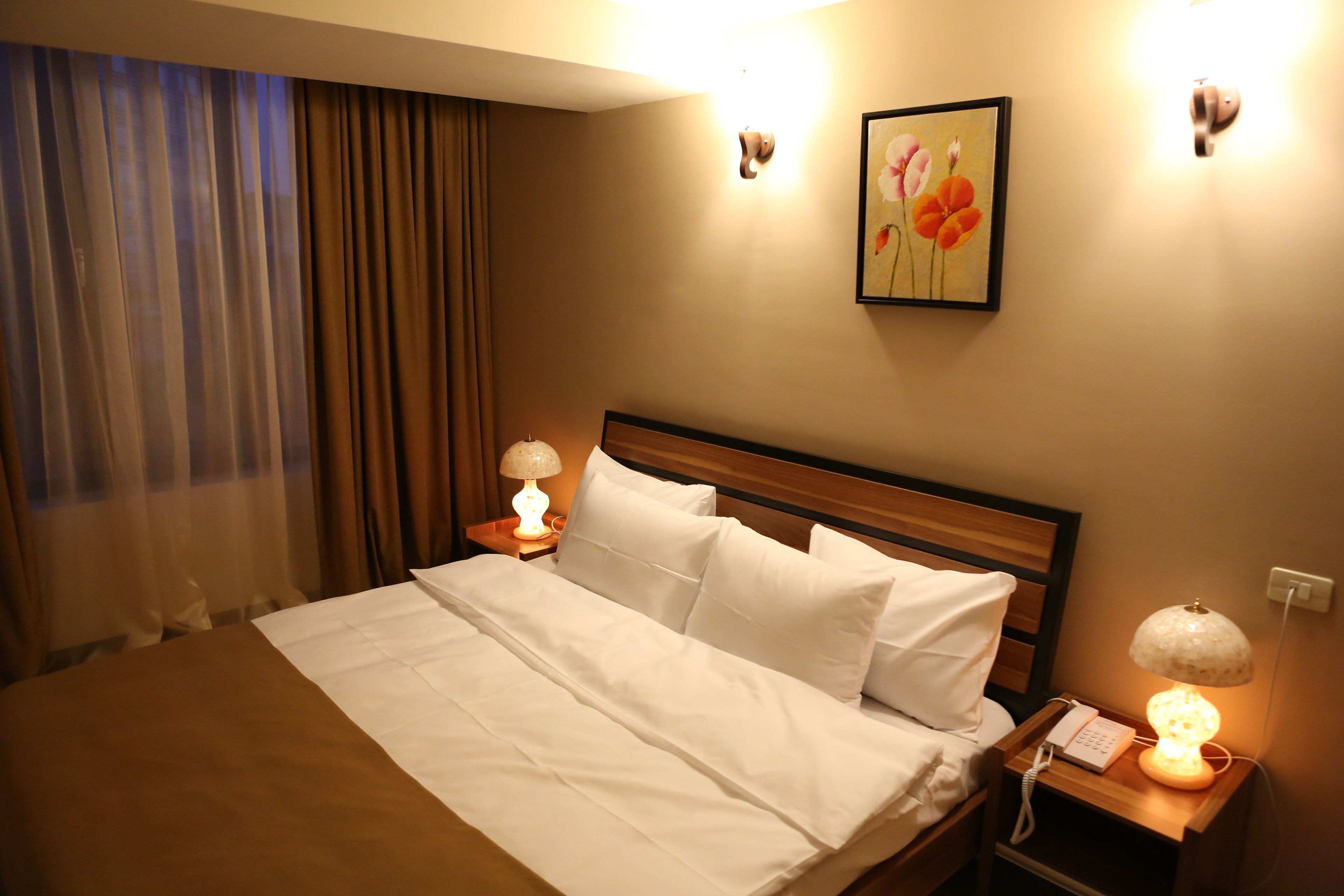 A hotel room with a neatly made bed, two bedside lamps, a nightstand with a phone, and a painting on the wall.