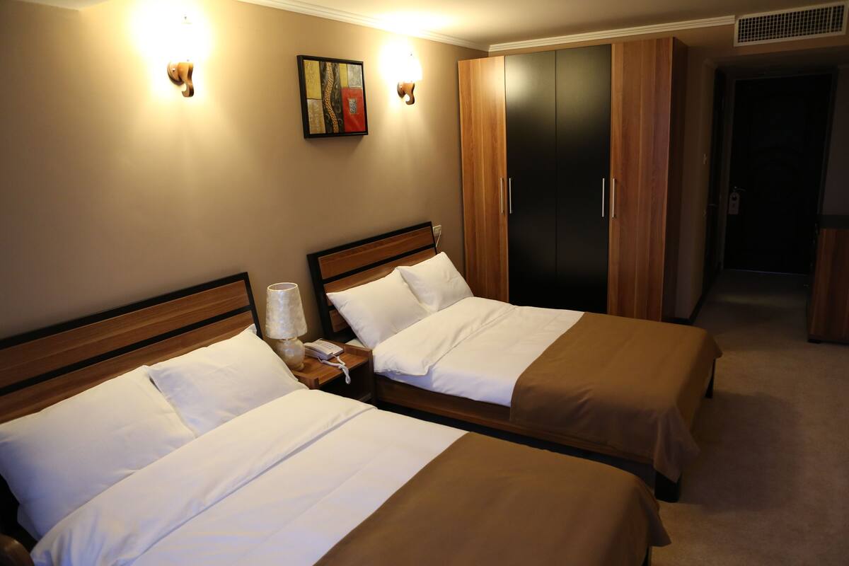 Une chambre d’hôtel avec deux lits, une table de chevet, une lampe, un tableau au mur et une armoire.