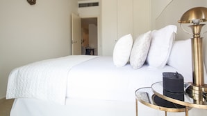 A neatly made bed with white linens, a bedside table with a lamp, and a door leading to another room. - Splendom Suites Pau Claris (Barcelona)