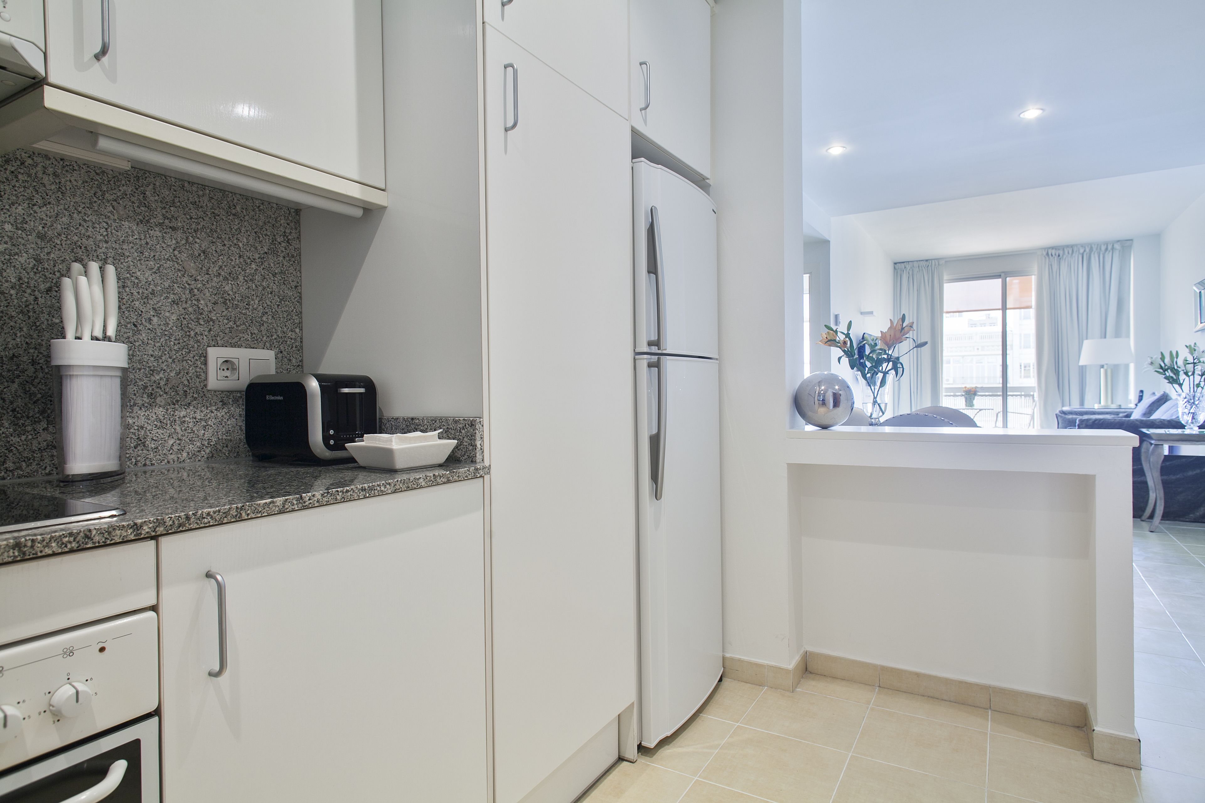 A modern kitchen with white cabinets, a granite countertop, and a built-in refrigerator.