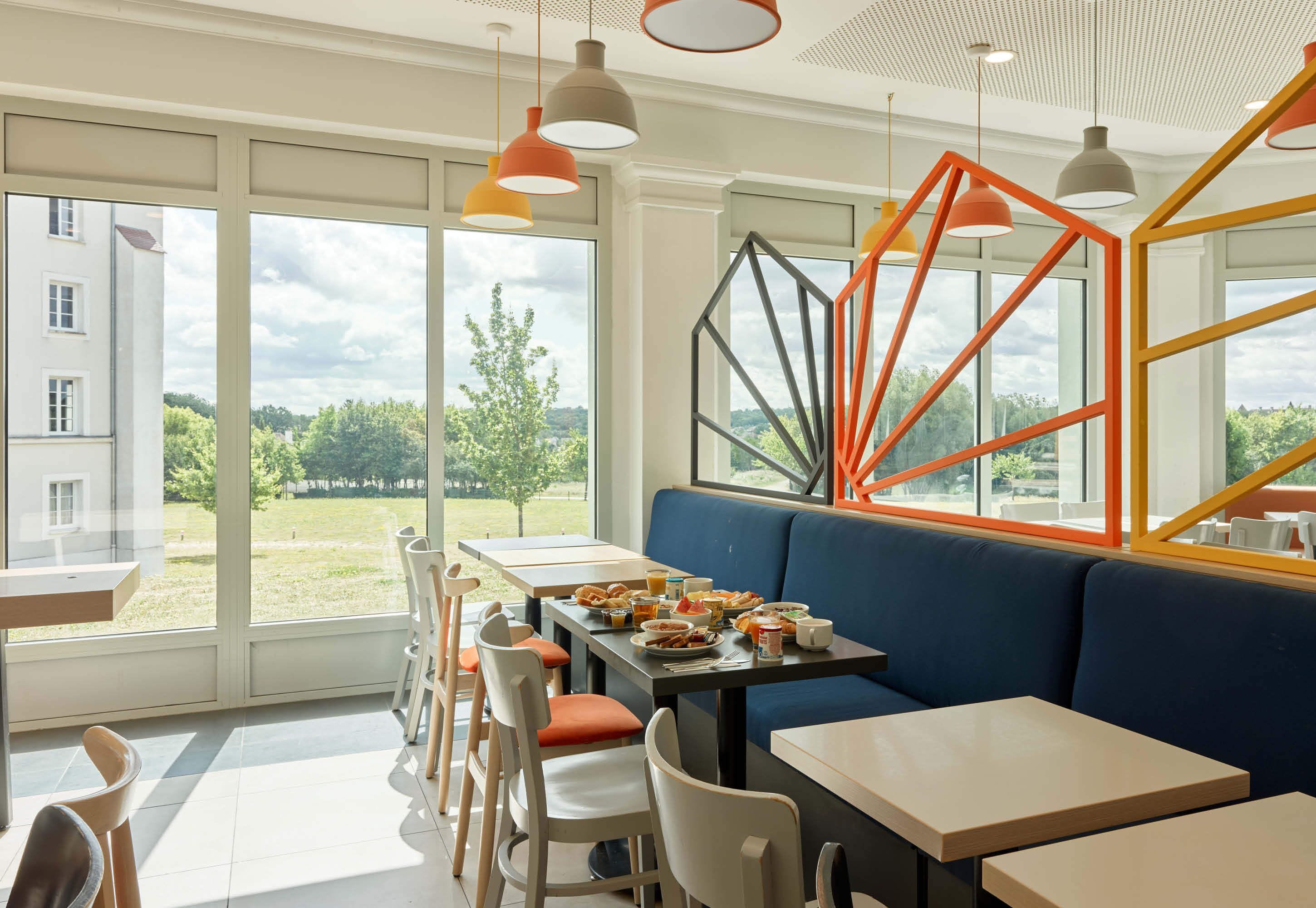 A modern dining area with large windows, a blue sofa, and orange pendant lights.