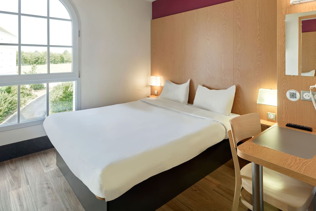 Une chambre d’hôtel avec un grand lit, des lampes de chevet, un bureau et une vue sur la verdure.