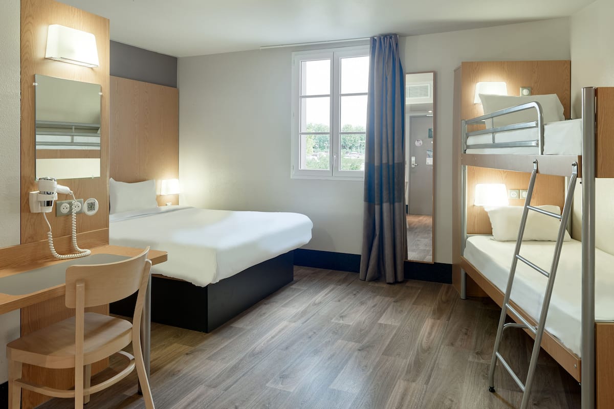 Une chambre d’hôtel avec un lit, un bureau, une chaise, des lits superposés et une fenêtre avec des rideaux.