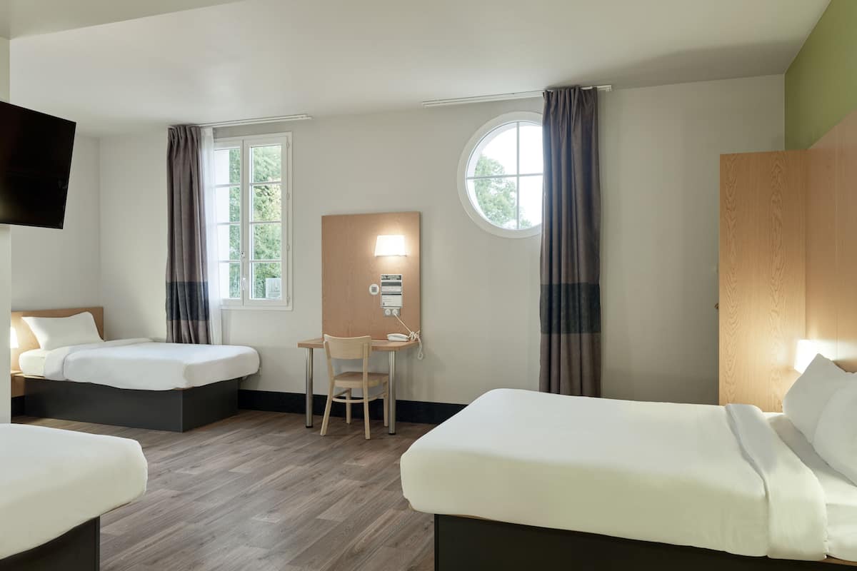 Une chambre d’hôtel avec deux lits, un bureau, une chaise, une télévision et une fenêtre avec des rideaux.
