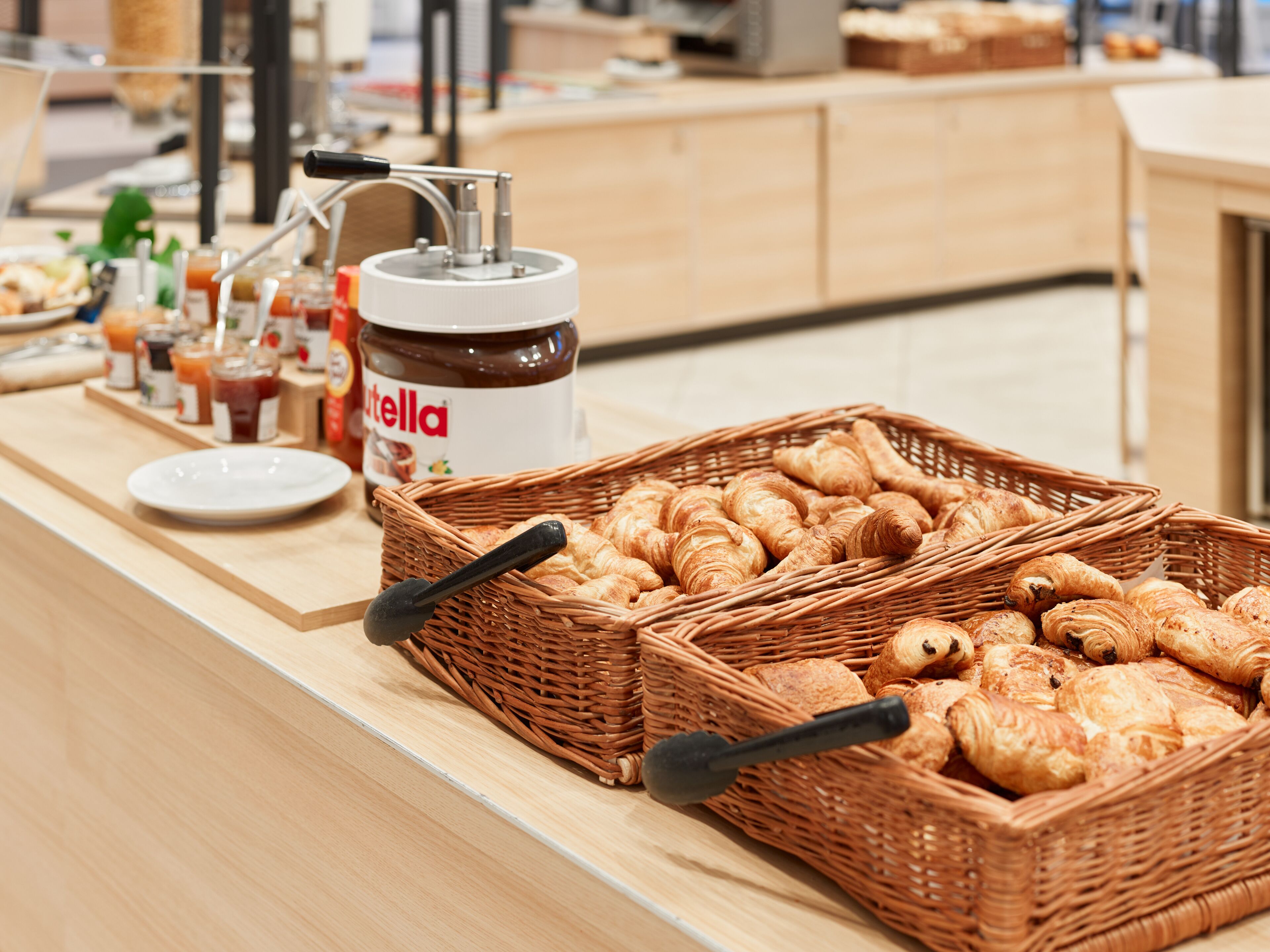 Una mesa de buffet con canastillas de croissants y un tarro de Nutella.