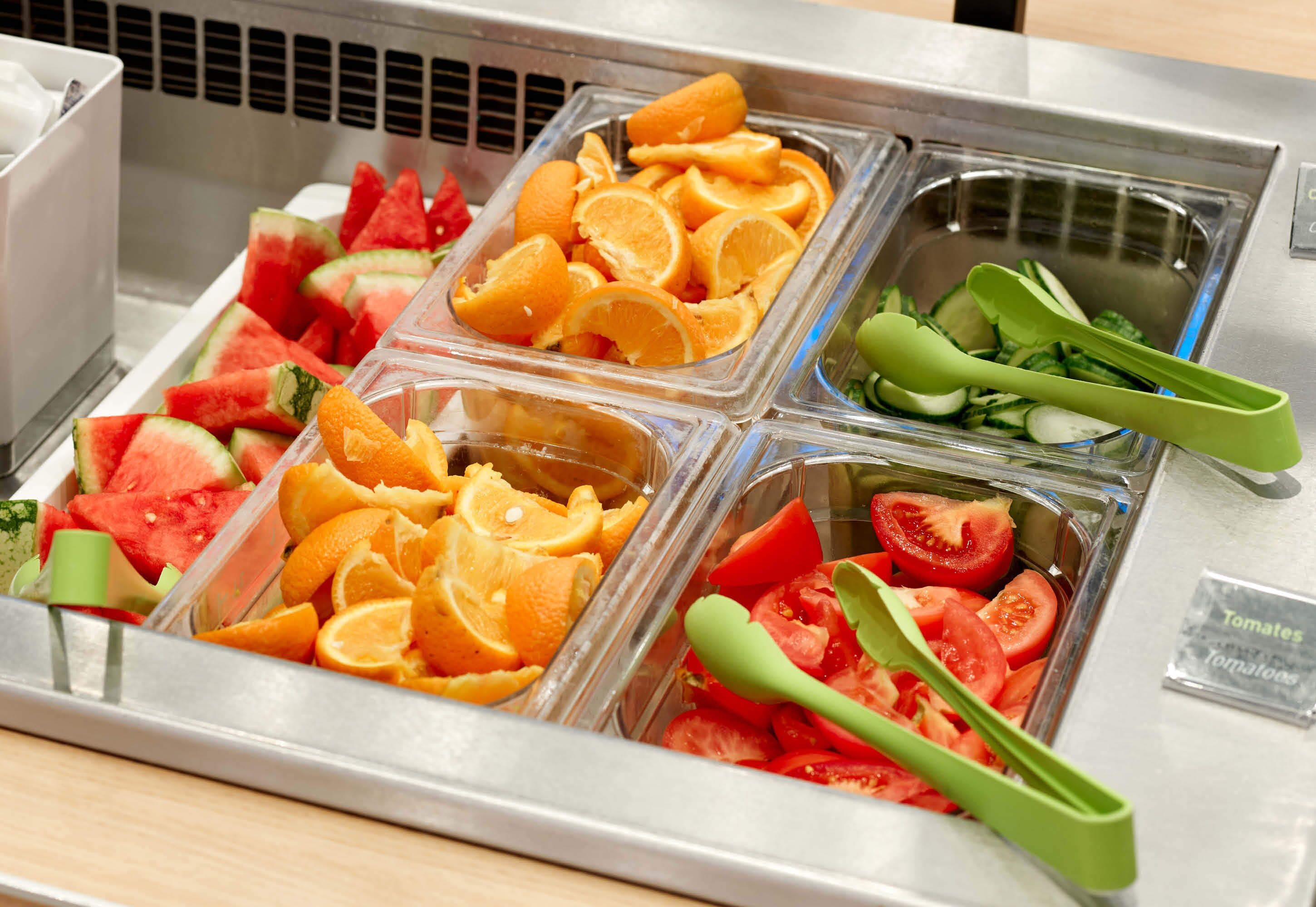 Exhibición de alimentos con frutas y verduras en recipientes transparentes.