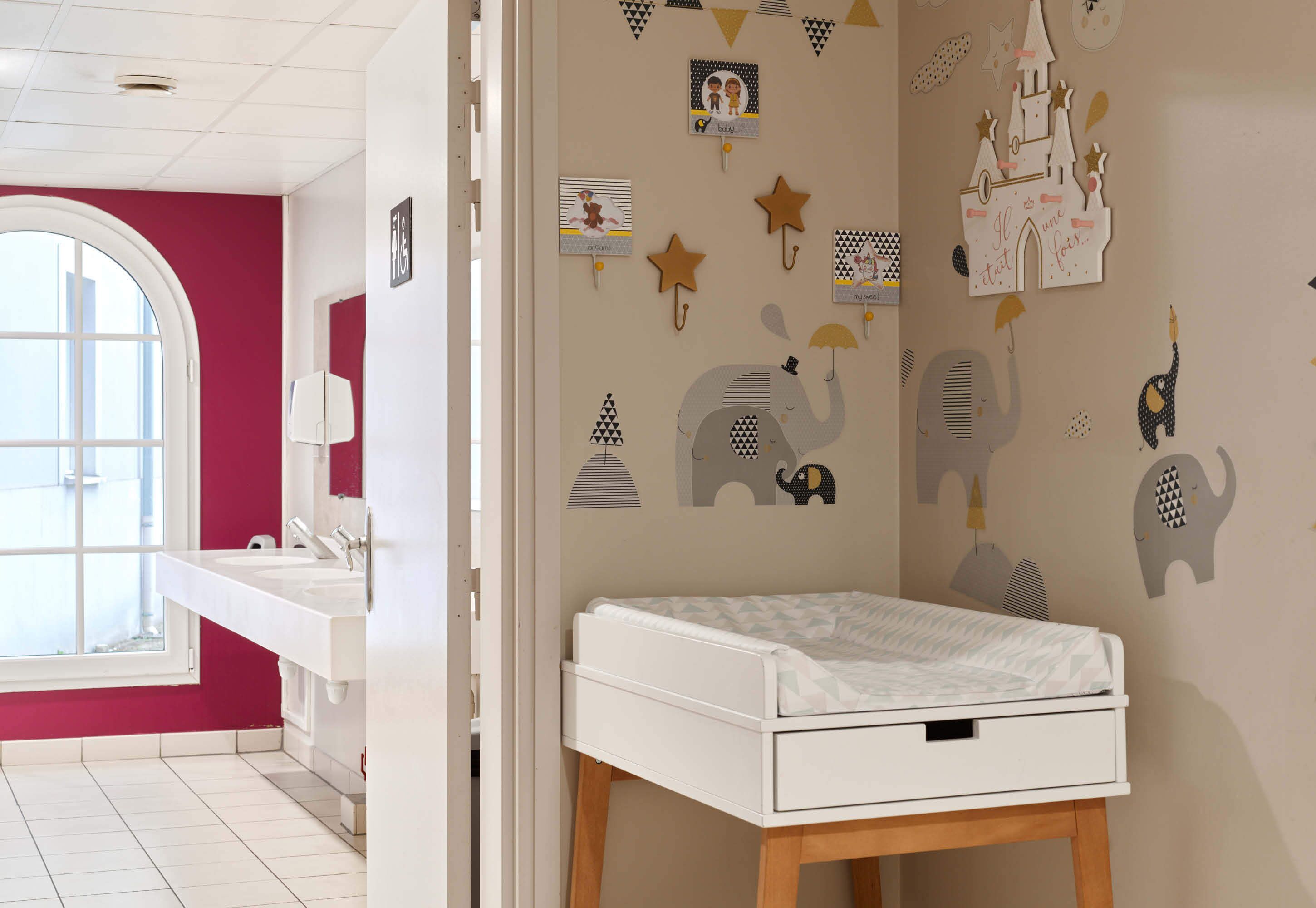 Een kinderkamer met een ledikant, een raam en wanddecoraties, waaronder sterren en dierenfiguren.