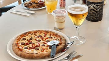 A pizza on a plate with a pizza cutter, a glass of beer, and a milkshake on a table.