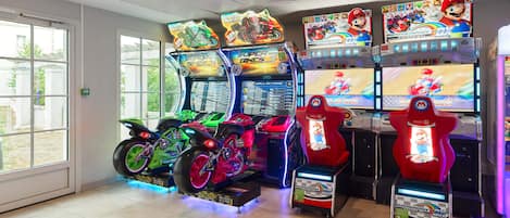 A row of arcade games including Mario Kart and Super Bikes, with a view of the outside through large windows.