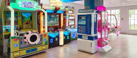 Una fila di luminosi cabinati da gioco in un'ampia area interna con pavimento piastrellato e grandi finestre che lasciano entrare la luce naturale.