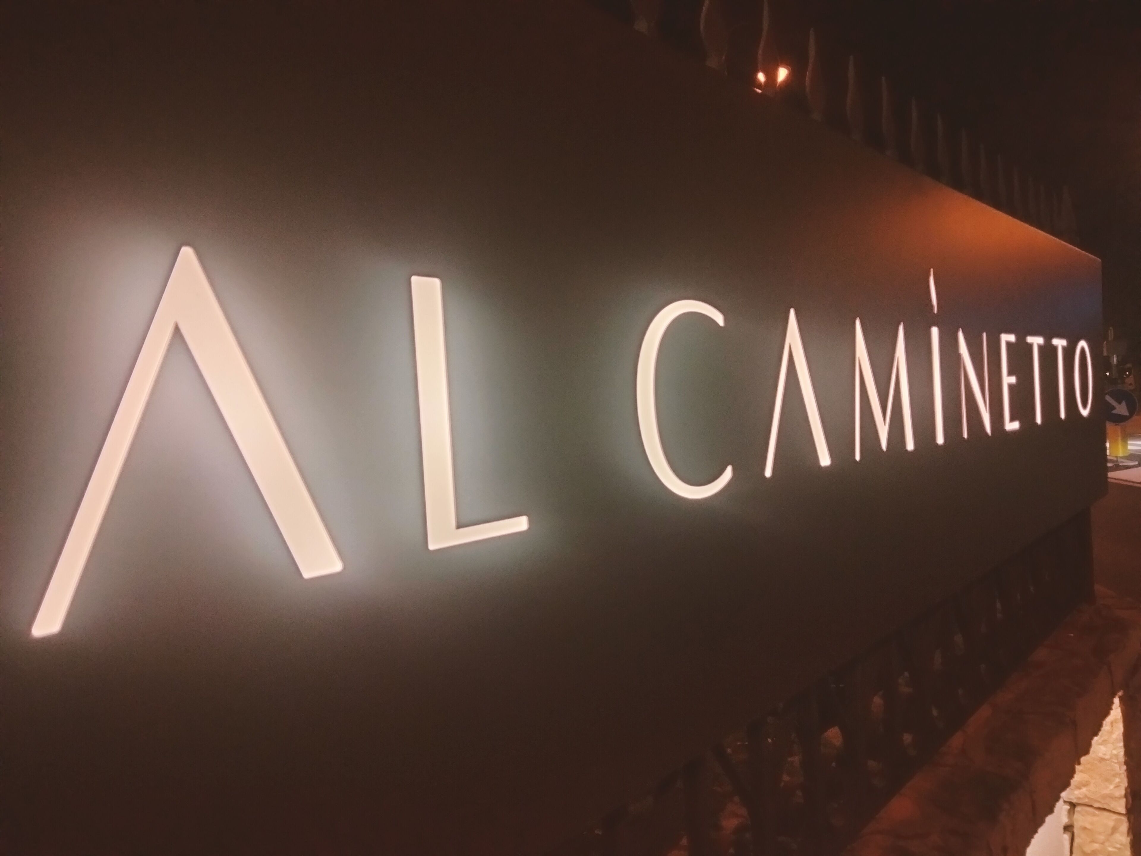 A sign with the name "AL CAMINETTO" illuminated in white letters.