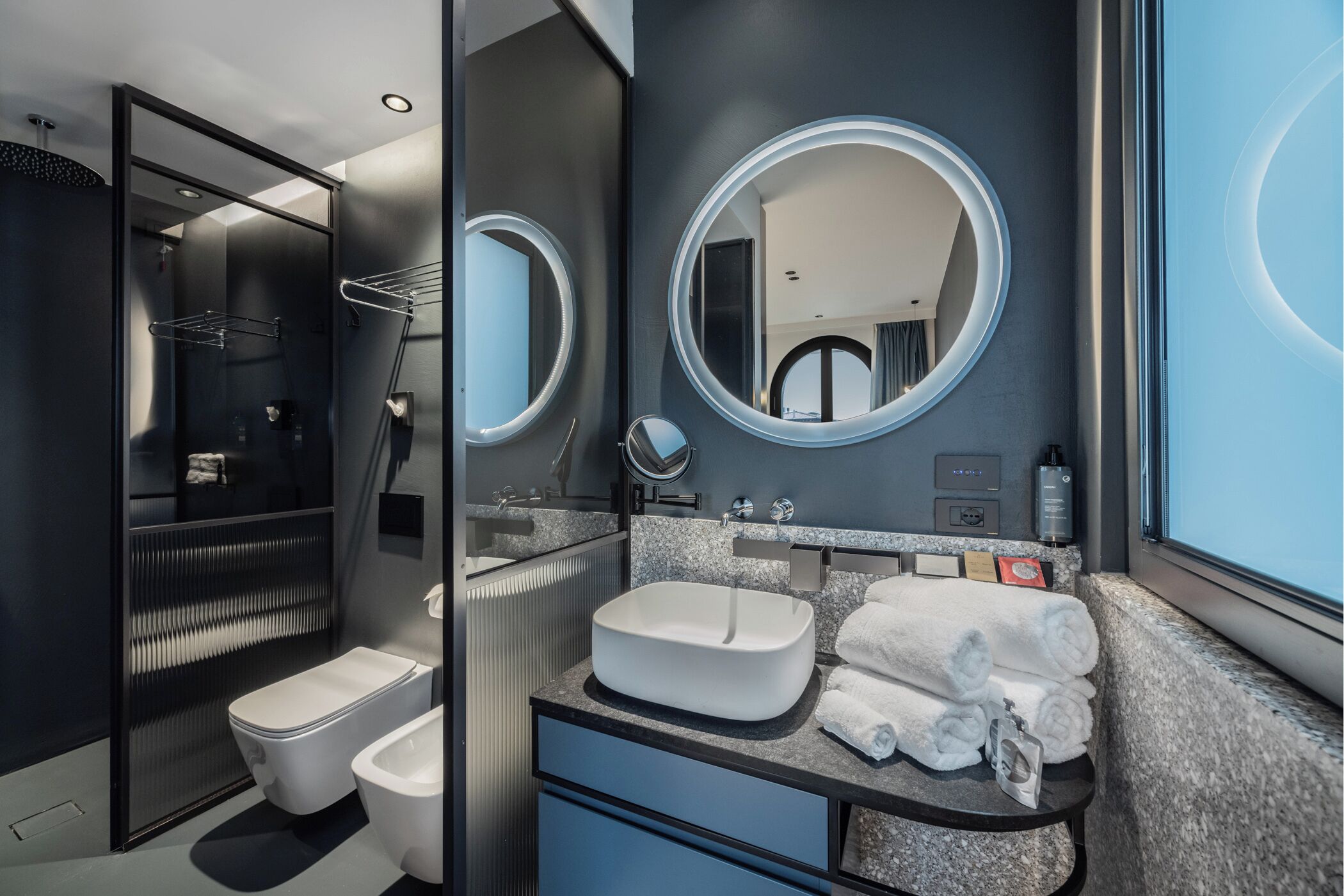A modern bathroom with a toilet, bidet, and sink, featuring a large mirror and towel rack.