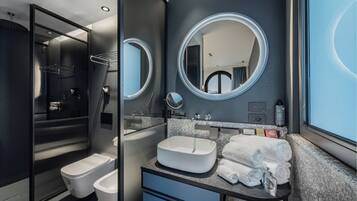 A modern bathroom with a toilet, bidet, and sink, featuring a large mirror and towel rack.