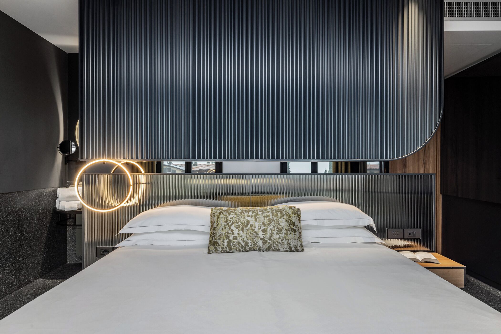 A modern bedroom with a large bed, a round mirror, and a headboard with vertical lines.