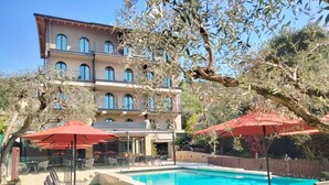 A pool area with lounge chairs and umbrellas, surrounded by a building with multiple balconies and olive trees. - Hotel Al Caminetto – Adults Only, WorldHotels Crafted (Torri del Benaco)