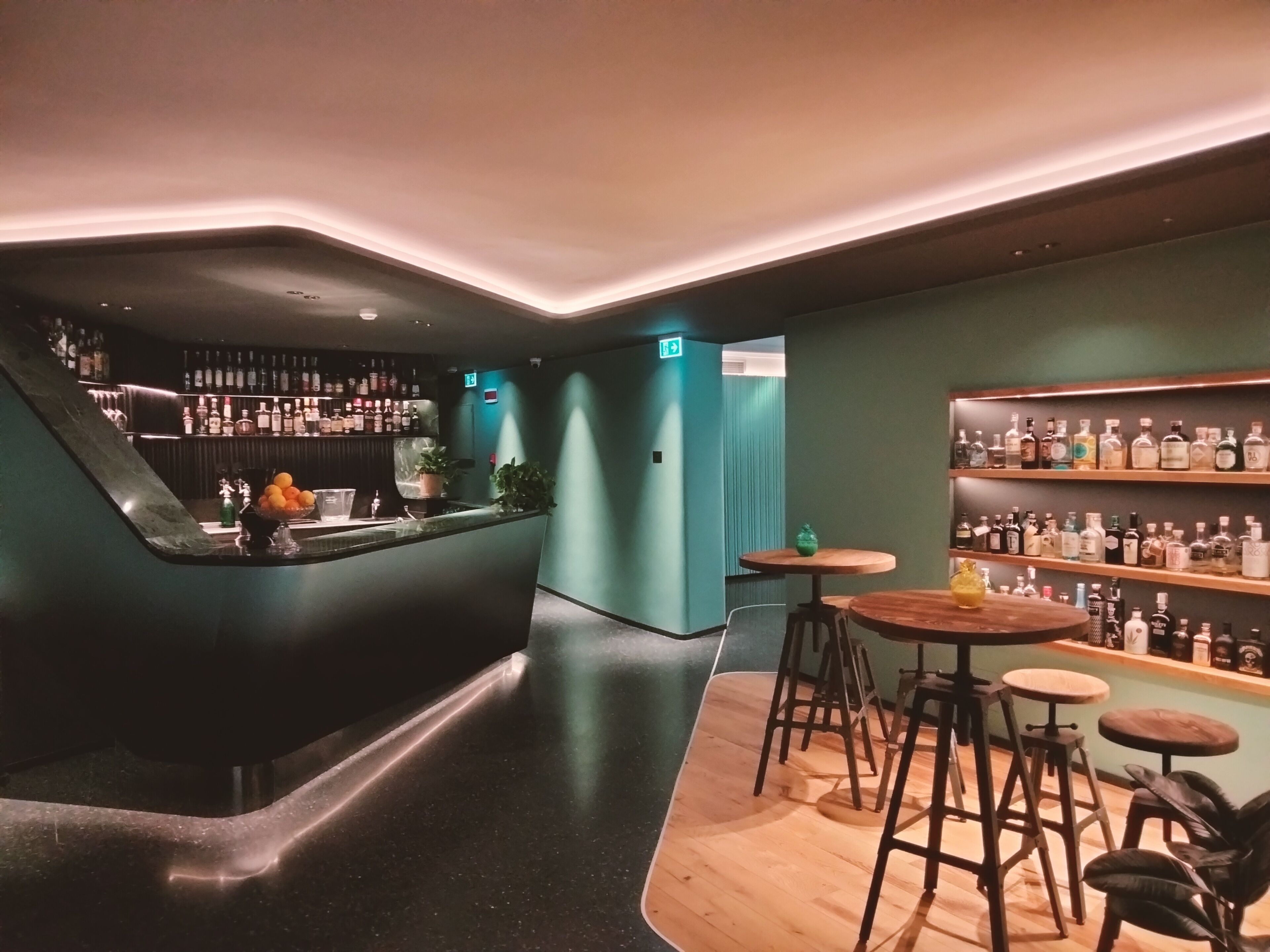 A bar area with a counter, stools, and shelves of bottles.