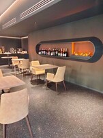 Interior moderno de restaurante con una larga vitrina de botellas de vino, chimenea y una zona de estar con mesas y sillas.