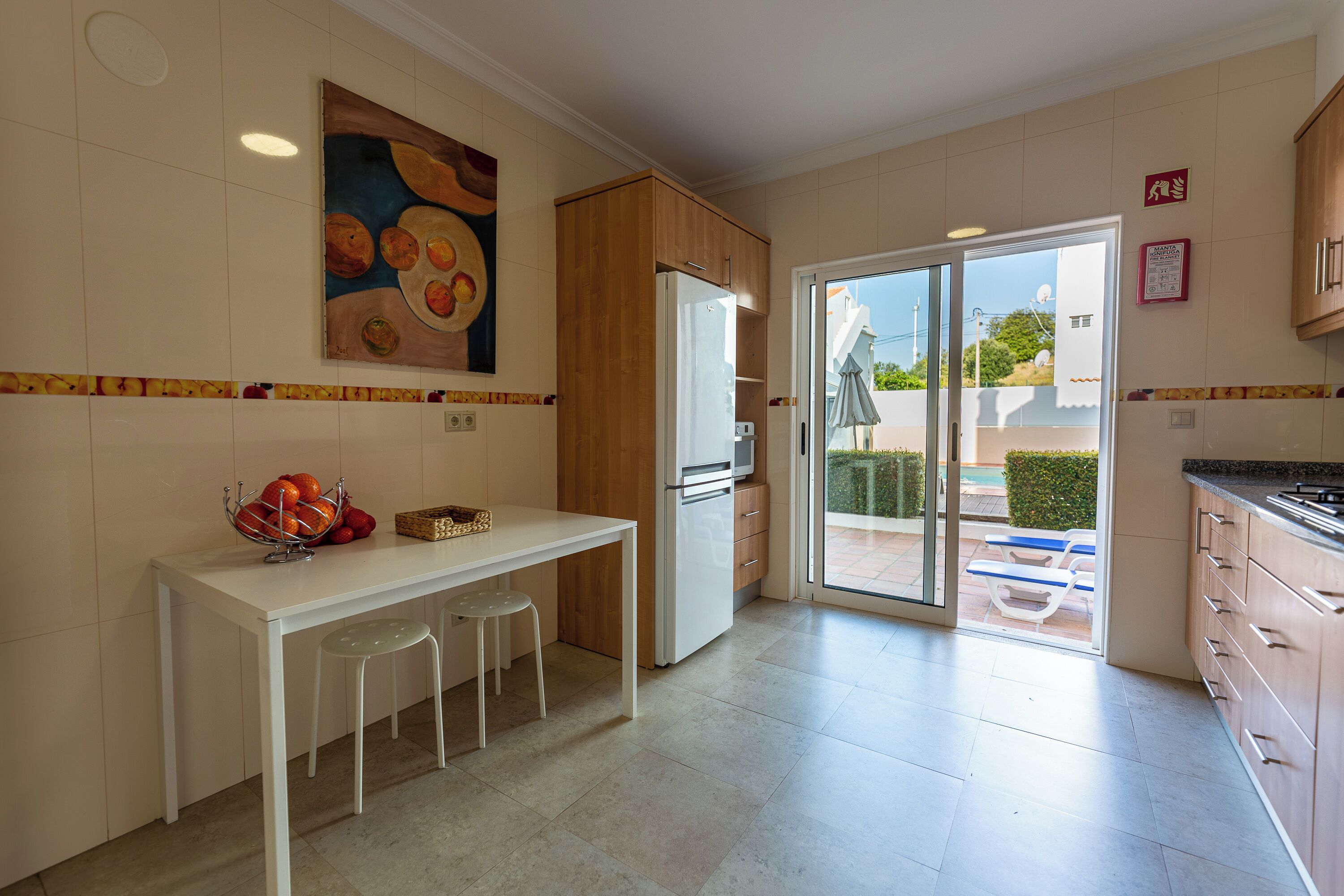 A modern kitchen with a white countertop, wooden cabinets, and a dining area with stools.