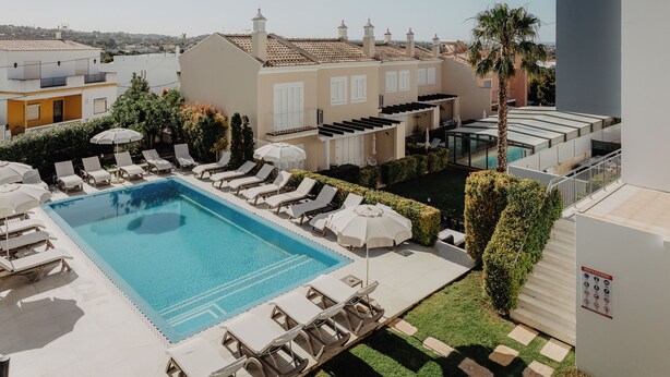A rooftop pool with lounge chairs and umbrellas, surrounded by buildings and a palm tree. - Boutique e Villas Boliqueime (Loulé)