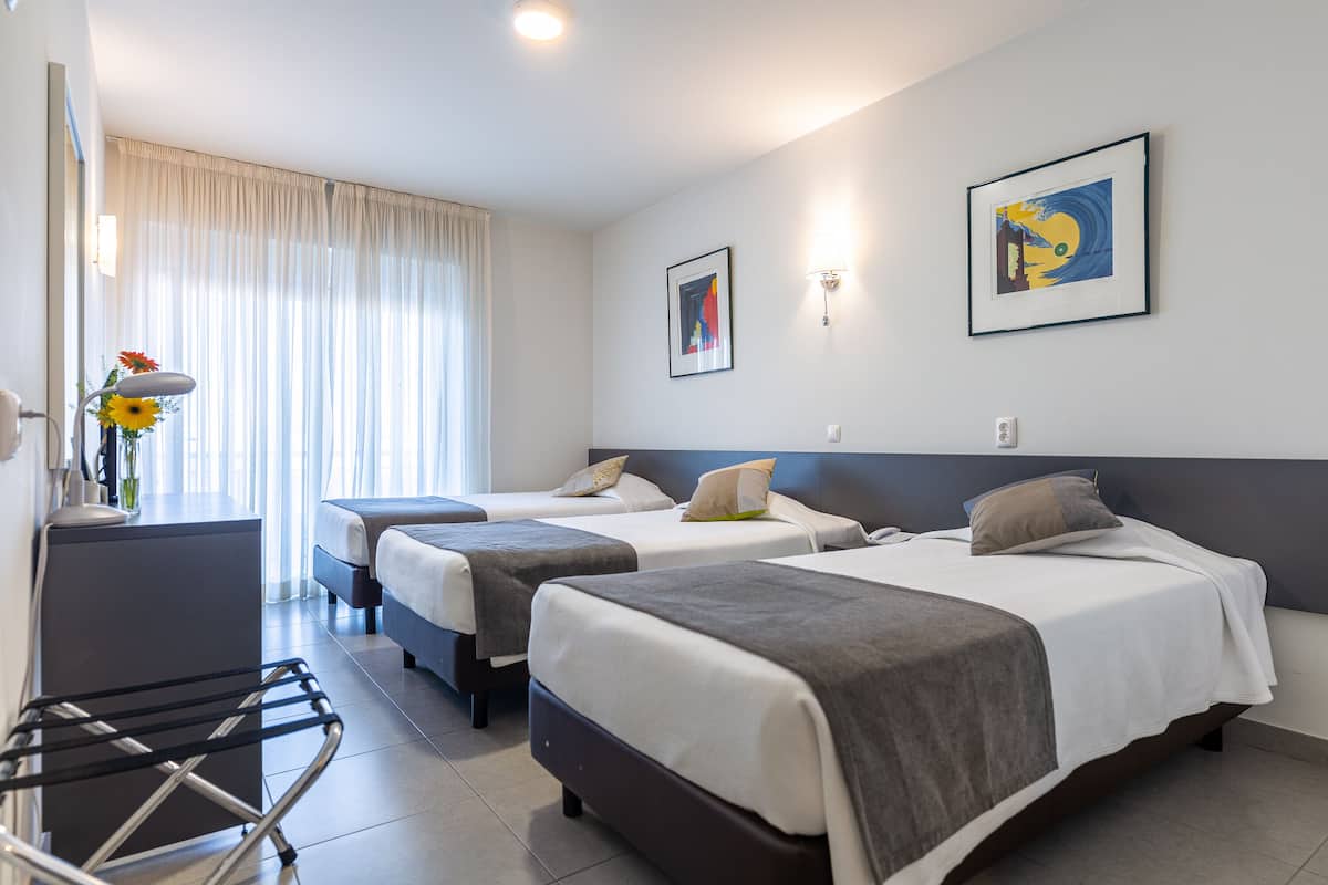 A hotel room with two beds, a desk, a chair, and a window with curtains.