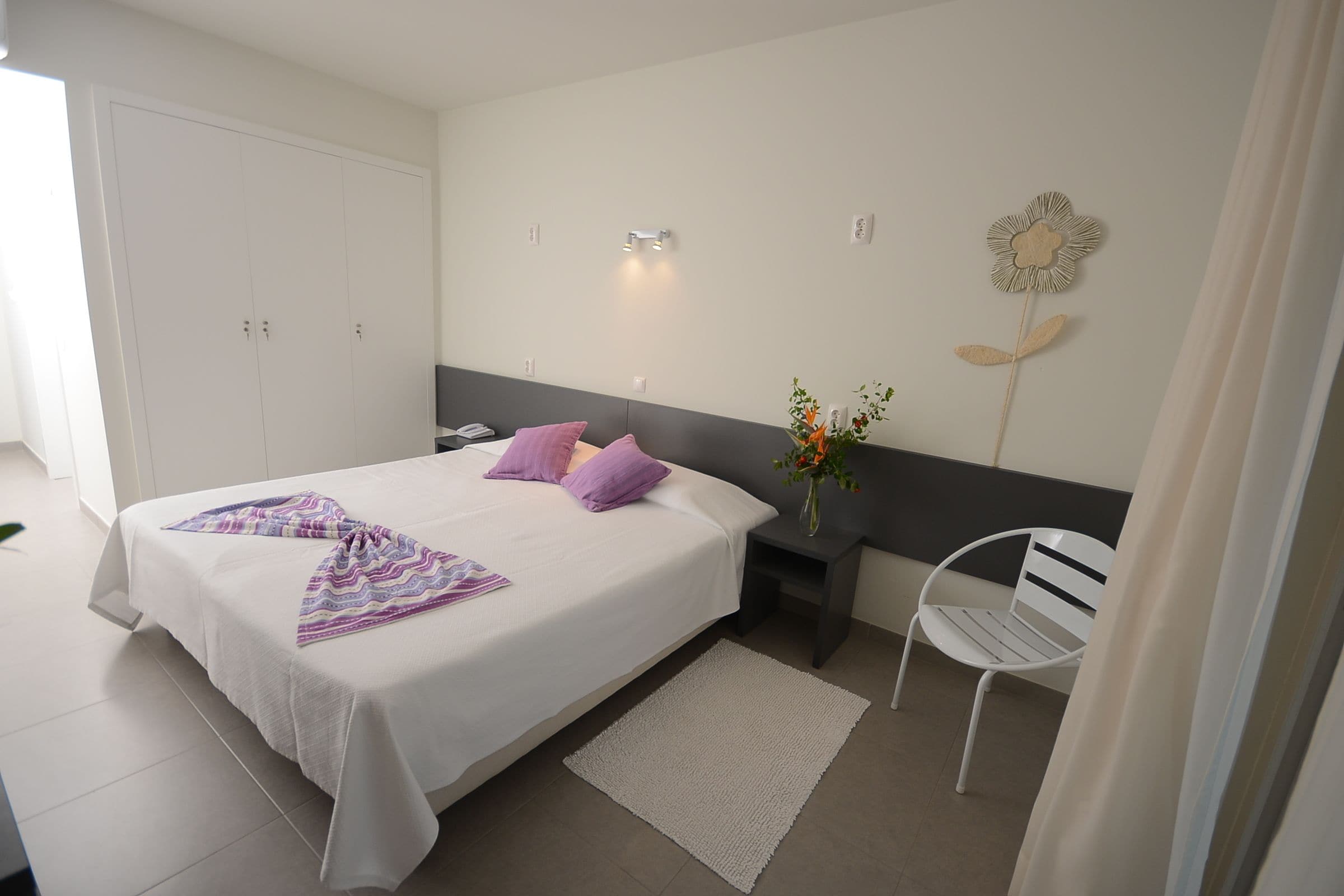 A neatly arranged bedroom with a bed, bedside table, chair, and a wall-mounted flower decoration.