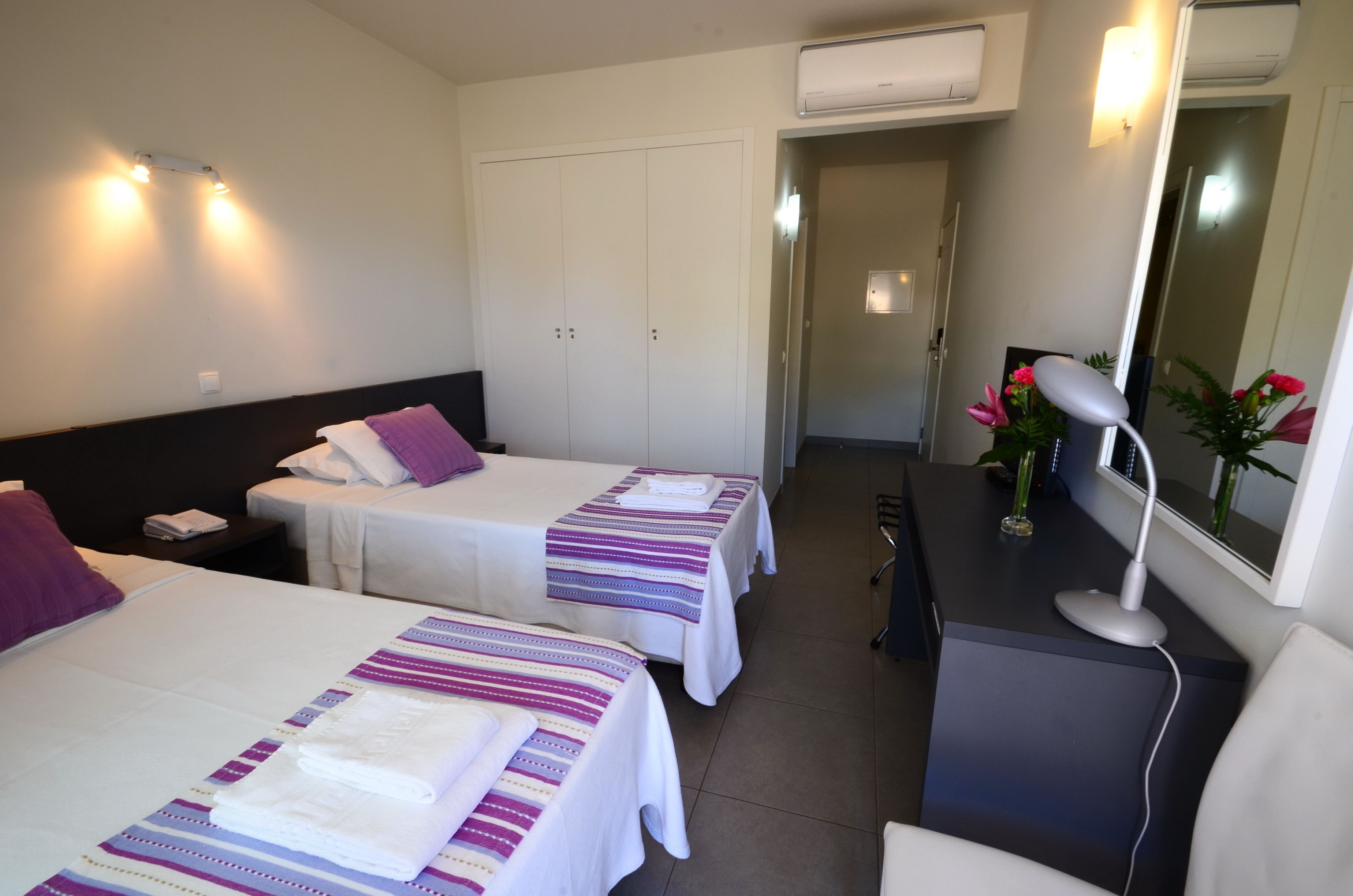 A hotel room with two beds, a desk, a chair, a mirror, and a nightstand.