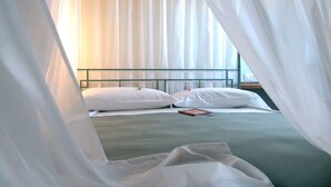 A bed with white linens and a green bedspread, a bedside table with a book, and sheer curtains. - Corte Uccellanda (Monzambano)