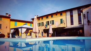 A pool area with a gazebo, outdoor umbrellas, and a building with multiple windows and balconies. - Corte Uccellanda (Monzambano)