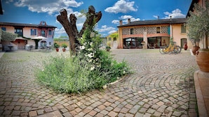 A courtyard with cobblestone paving, a large tree, and buildings with balconies and outdoor seating. - Corte Uccellanda (Monzambano)