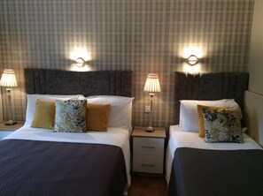 Camera d'albergo con due letti, ciascuno dotato di poggiatesta, comodini, lampade e cuscini decorativi.