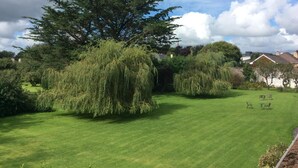 A well-maintained lawn with a large tree and shrubbery, a clear sky, and a residential building in the background. - The Gardens guest accommodation (Killarney)