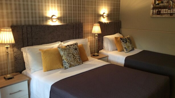 A hotel room with two beds, a nightstand with a lamp, and a wall-mounted light fixture. - The Gardens guest accommodation (Killarney)