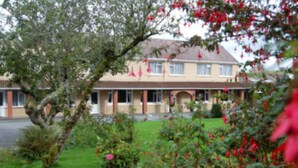 A two-story building with a symmetrical facade, a central entrance, and a small porch area. - The Gardens guest accommodation (Killarney)