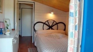 A bedroom with a bed, a nightstand, a lamp, and a door leading to another room. - Hôtel du Marché (Beauvoir-sur-Mer)